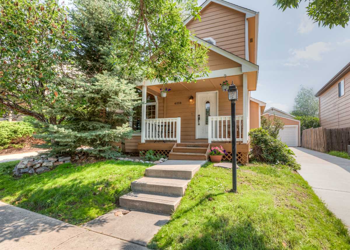Charming Victorian-style cottage with white picket fence and covered front porch surrounded by mature trees in Colorado Springs | Logo Inc Real Estate
